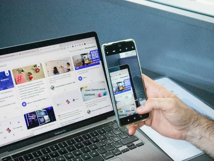 Un ordinateur portable affiche une page web, avec un smartphone tenu devant son écran