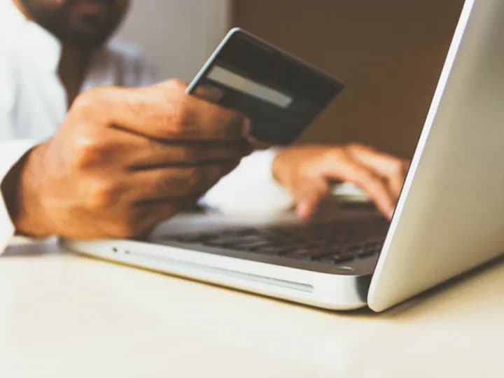 Une personne effectue un achat en ligne, carte bancaire en main devant son ordinateur portable